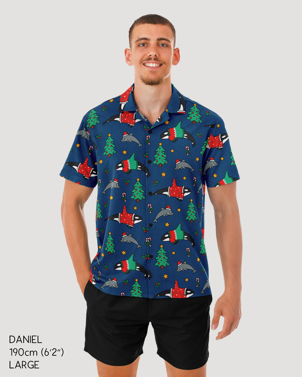 Man wearing a colorful patterned shirt with Christmas-themed designs on a plain background
