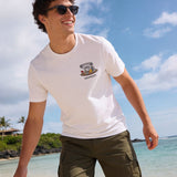Man wearing a white t-shirt with the Hammered Shark logo and olive cargo shorts standing on a beach.