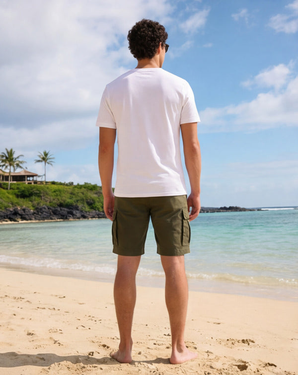 Man wearing a white t-shirt with the Hammered Shark logo and olive cargo shorts standing on a beach. Back view